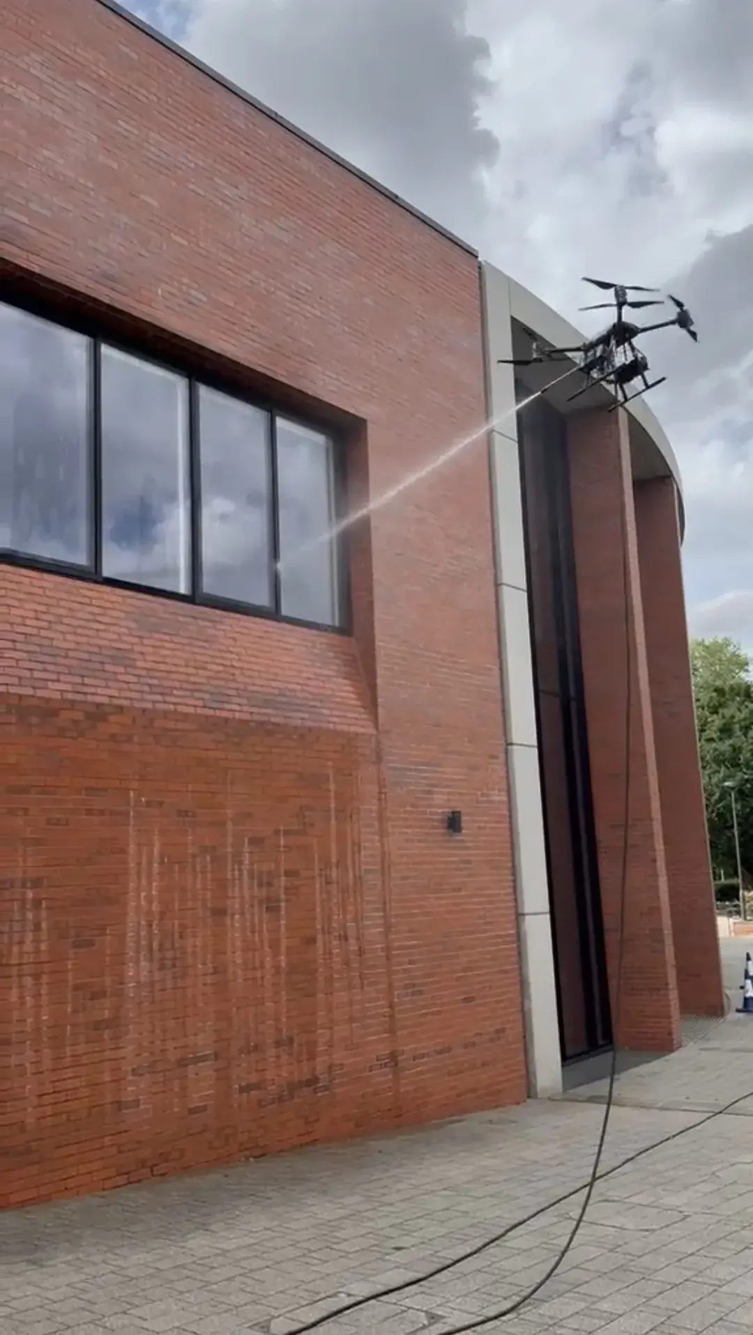 Drone spraying water to clean the windows of a brick building